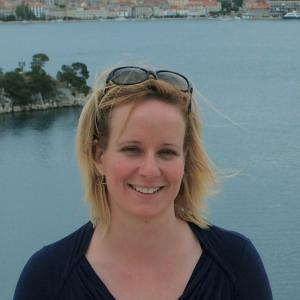 image of Sarah McClure from the shoulder up standing in front of the water in a black shirt, smiling